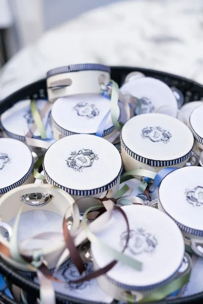Wedding favors in round favor boxes with striped ribbon trim and monogram labels, arranged in a basket on soft white fabric backdrop