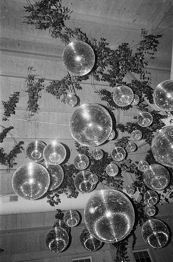 Disco ball decor with hanging disco balls and greenery garlands suspended on wires beneath a wood-beam ceiling canopy