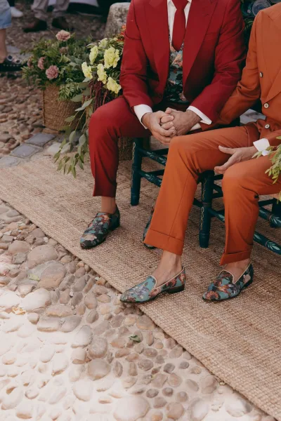Groom shoes, men's wedding loafers, poised on a jute rug aisle along a cobblestone path, with wooden chairs, greenery, and floral arrangements.