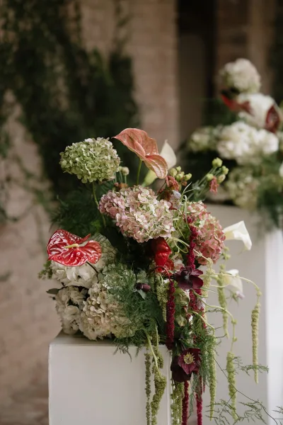 Wedding floral arrangement styled as a pedestal flower arrangement, featuring sculptural anthurium, set against a brick wall with climbing vines.