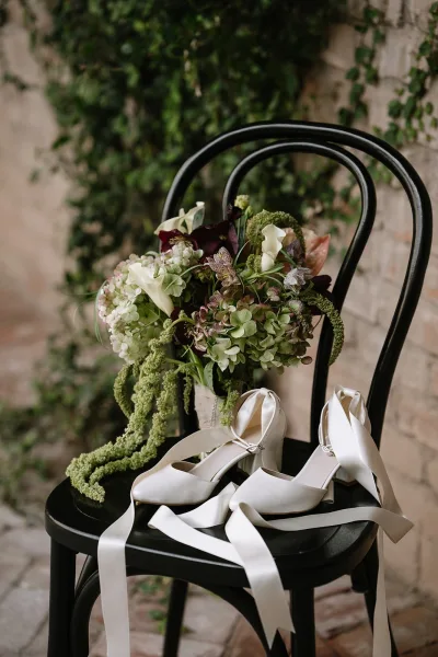 Wedding bouquet styled as a cascading bridal bouquet rests on a black chair before a brick wall with ivy vines.