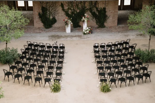 Ceremony setup with modern ceremony seating and black bentwood chairs facing an ivy-covered brick wall in a courtyard.