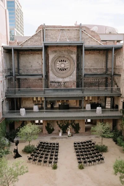 Ceremony setup for an outdoor courtyard ceremony with aisle candles beneath exposed brick walls and steel beams in an urban courtyard venue.