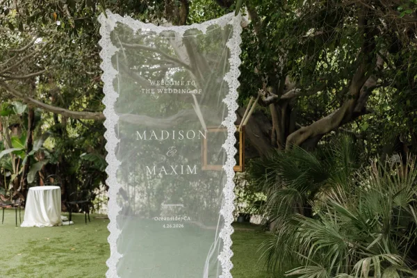 Wedding welcome sign on sheer fabric, a fabric wedding sign set before garden trees and tropical plants.