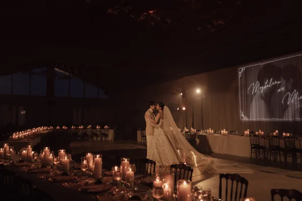 Wedding first dance as the couple slow dance amid candles in an indoor reception hall with softly draped walls.