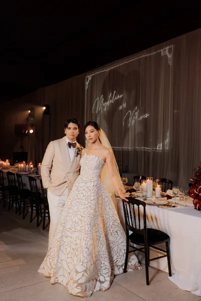 Couple portrait of the bride and groom at the reception, her strapless floral gown framed by a draped backdrop and a projected monogram.