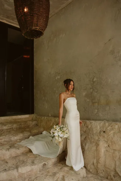 Bridal portrait of a bride in a strapless wedding dress with a calla lily bouquet, standing on stone steps by a textured wall