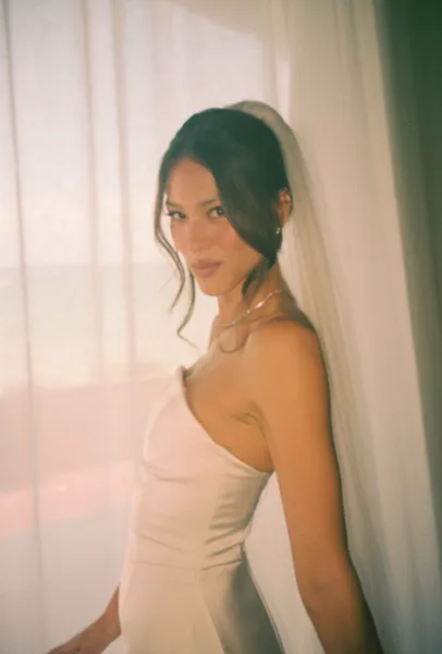 Bridal portrait with a bridal veil, bride in a strapless wedding dress and necklace, softly lit by window light near sheer curtains