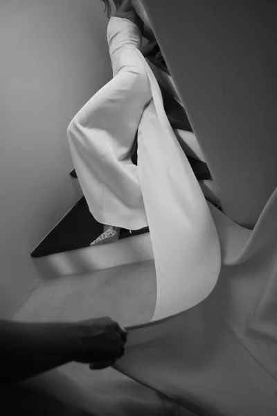 Bridal gown in a satin wedding dress with a long train draped on a staircase, paired with high heels in a white hallway