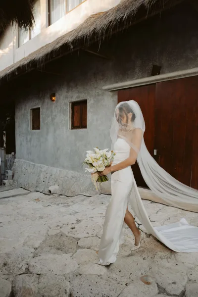 Bridal portrait of a bride in a strapless wedding dress with cathedral veil and calla lily bouquet, walking past wooden doors in a stone courtyard