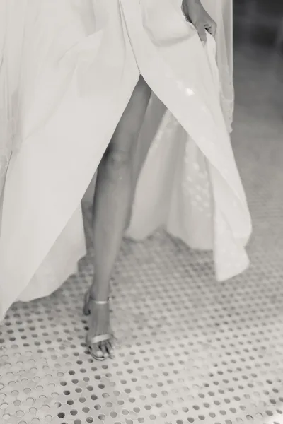 Wedding dress slit reveals bridal shoes detail as ankle-strap heels peek from a minimalist gown, capturing clean, modern elegance.