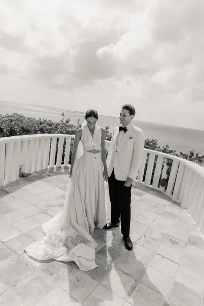 Couple portrait in an ocean view wedding photo, bride in a simple veil beside her groom on a tiled terrace by a curved railing.