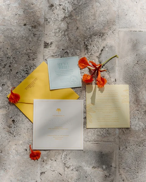 Wedding invitation suite for tropical wedding invitations, arranged with flower petals on textured stone tile.