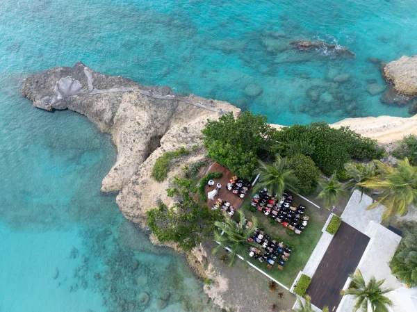 Oceanfront ceremony setup for a cliffside wedding ceremony on a wooden platform, facing a turquoise ocean with rocky shoreline and swaying palms.