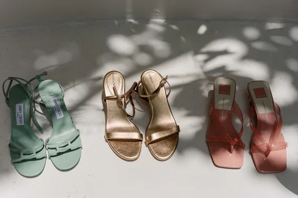 Bridal shoes—mint green wedding heels with a square toe—rest on a white floor as dappled sunlight casts soft leaf shadows around them.
