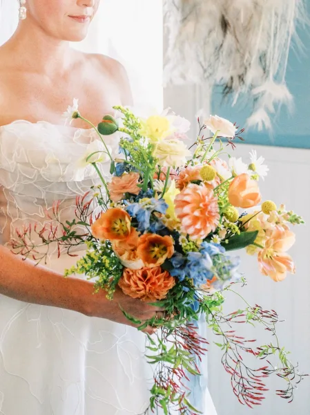 Bridal bouquet, a peach and blue bouquet with a trailing ribbon, set before pampas grass and blue and white walls.
