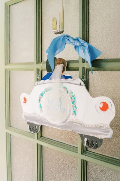 Wedding sign styled as a just married sign, trimmed with a blue ribbon bow, hangs on a green paneled door with frosted glass panes in soft light.