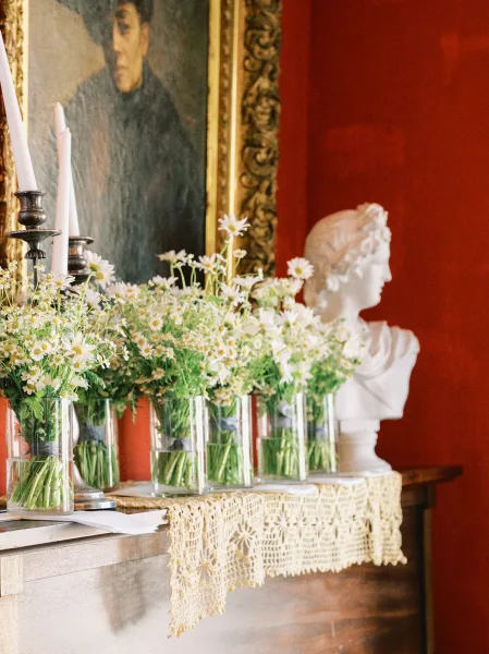 Mantel wedding decor featuring fireplace mantel wedding flowers and taper candles on a wood mantel against a red wall with a gold-framed painting.
