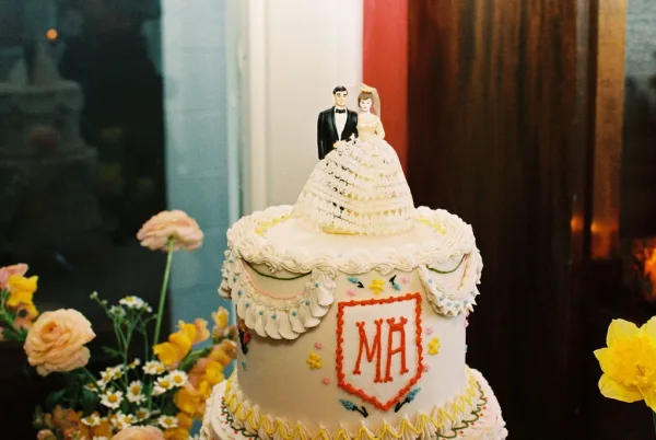Wedding cake with intricate buttercream piping, displayed by a window against wood paneling in an indoor setting