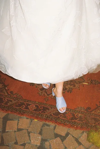 Bridal shoes, elegant blue wedding shoes with delicate floral embroidery, rest on a patterned rug atop mossy cobblestone.