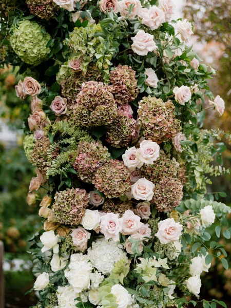 Ceremony florals in a floral column wedding design with roses, creating an installation set amid garden greenery and trees.