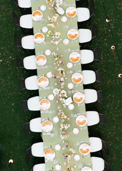 Reception tablescape on a long reception table with orange menu cards, set on a grass lawn under twinkling string lights.