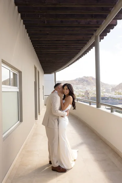 Couple portrait as the bride and groom embrace on a columned balcony, showcasing her engagement ring against a city skyline and mountains.