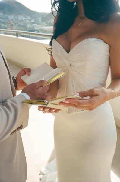 Wedding vows, with the couple exchanging vows and holding vow books on a balcony overlooking a cityscape and rolling hills.