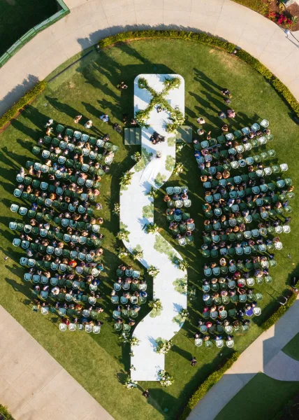 Ceremony setup with an outdoor wedding ceremony white aisle runner in an S-shaped curve, lined with greenery garland and florals on a grass lawn