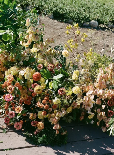Wedding floral arrangement with cascading garden flowers and greenery foliage, set low along a garden path on lawn grass beside soil beds