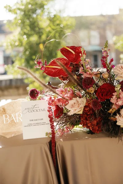 Signature cocktail sign for a wedding bar menu, styled with anthurium blooms beside the display on a neatly dressed bar tabletop.