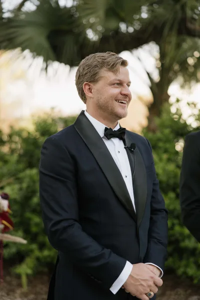 Groom portrait of a black tuxedo groom wearing a bow tie against palm leaves and garden greenery, crisp and classic.