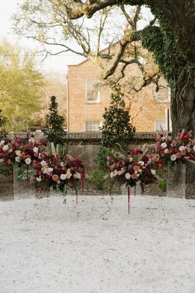 Ceremony altar decor as a lush garden ceremony backdrop on acrylic stands beneath a sprawling tree by an ivy-clad brick building