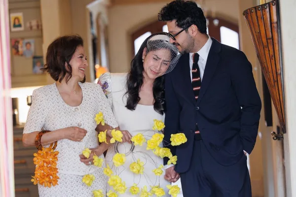 Ceremony moment of the bride, walking down the aisle with her groom and mother, wearing a birdcage veil and holding hands.
