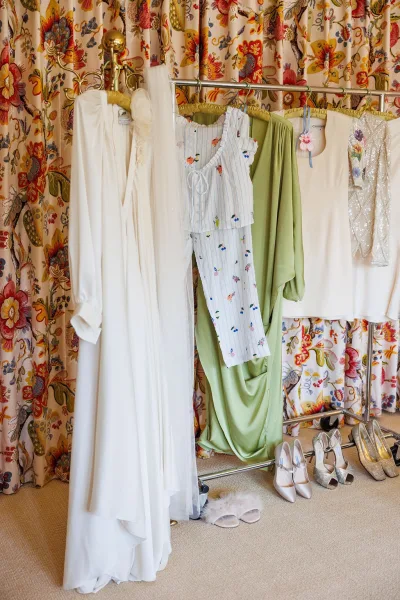 Getting ready details featuring a wedding dress on hanger with a veil, framed by floral curtains above a carpeted floor.