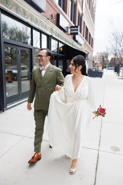 Couple portrait on a city sidewalk—an urban wedding portrait with the bride’s veil trailing and storefront windows behind.