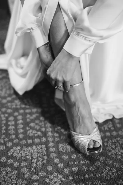 Bride putting on shoes in a quiet bridal getting ready moment, deftly fastening ankle-strap heels with graceful poise