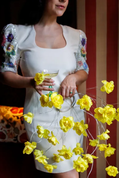 Bridal bouquet styled as a yellow wedding bouquet with wired stems creating airy, floating blooms, set indoors against a bold striped wall.