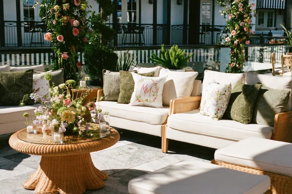 Wedding lounge with reception lounge seating on a patio terrace with balcony railing, centered around a rattan coffee table.