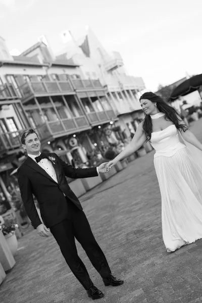 Couple portrait of the bride and groom walking down a cobblestone street lined with balconies and storefronts, his boutonniere adding a crisp detail.