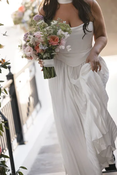 Bridal bouquet, a hand-tied bouquet of mixed florals with a trailing ribbon, held on a staircase with black railing and greenery.