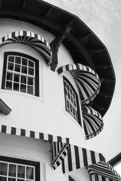 Building facade with a striped awning exterior on a rounded corner in white stucco, emphasizing classic black and white architecture.