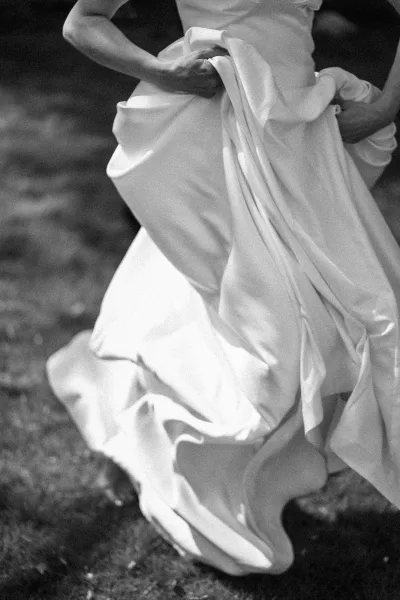 Wedding dress detail as a bride holding dress gathers the flowing gown, her hands guiding soft fabric folds