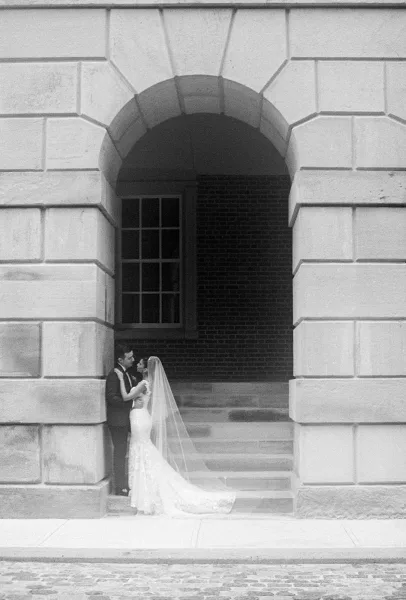 Wedding couple portrait in a black and white wedding photo, bride and groom embracing beneath a stone archway on cobblestone steps