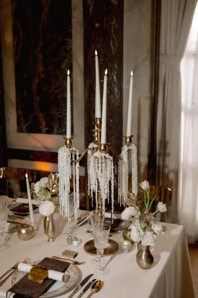 Reception tablescape with gold candelabra centerpiece, taper candles and white florals, set with menu cards by a marble wall mirror