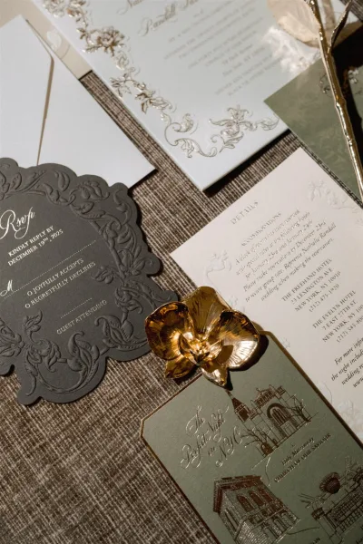 Invitation suite with foil stamped wedding invitations, embossed cards and envelopes, styled with a gold flower clip on linen fabric backdrop