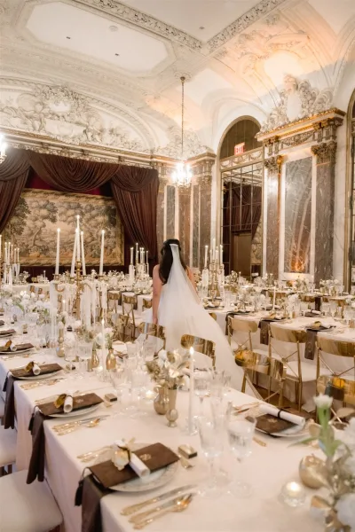 Reception tablescape with luxury wedding reception decor, taper candles and white florals on a long banquet table in an ornate ballroom with chandeliers