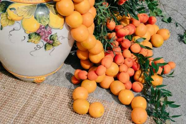 Citrus wedding decor arranged around a painted ceramic urn, offering fruit wedding ideas on a jute rug.