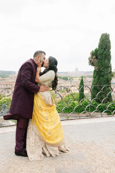 Wedding kiss portrait with yellow dupatta framing the bride, a city view couple photo on a terrace with a city skyline and cloudy sky.