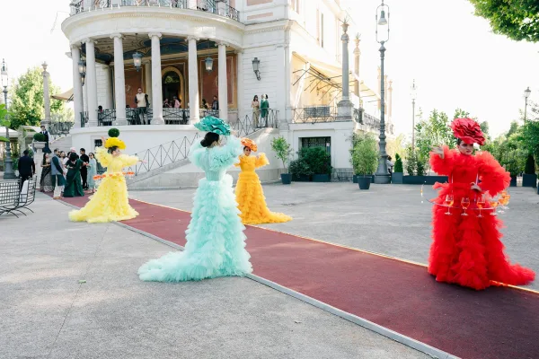 Wedding entertainment with cocktail hour performers presenting champagne on a red carpet before a historic building with columns.